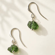 Raw drilled Chlum Moldavite earrings with naturally rounded green stones and rhodium-plated hooks.