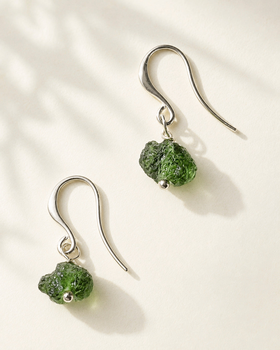 Raw drilled Chlum Moldavite earrings with naturally rounded green stones and rhodium-plated hooks.