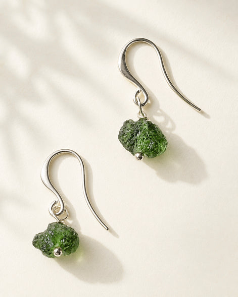 Raw drilled Chlum Moldavite earrings with naturally rounded green stones and rhodium-plated hooks.