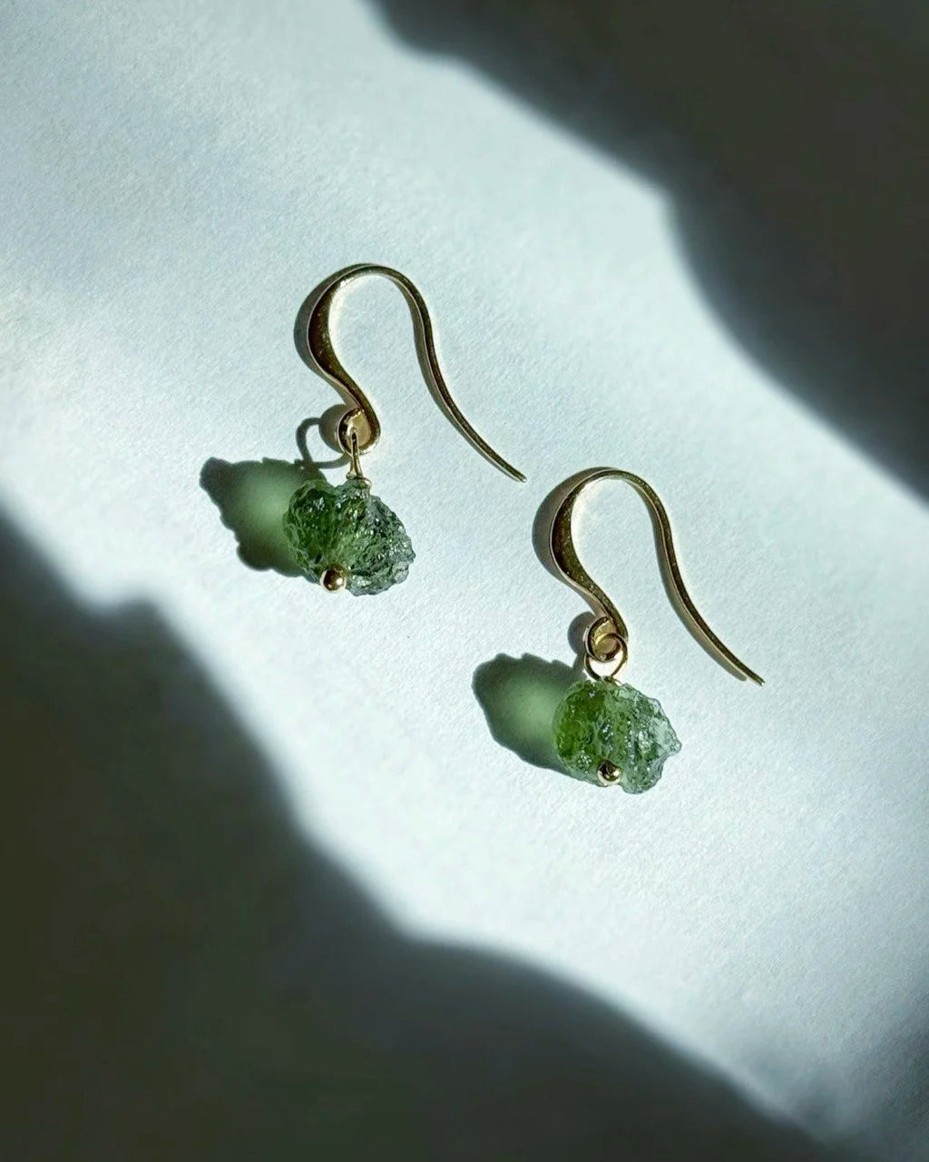 Raw drilled Chlum Moldavite earrings with naturally rounded green stones and gold-plated hooks.