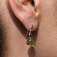 Raw drilled Chlum Moldavite earrings with naturally rounded green stones and rhodium-plated hooks.