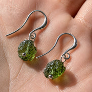 Raw drilled Chlum Moldavite earrings with naturally rounded green stones and rhodium-plated hooks.