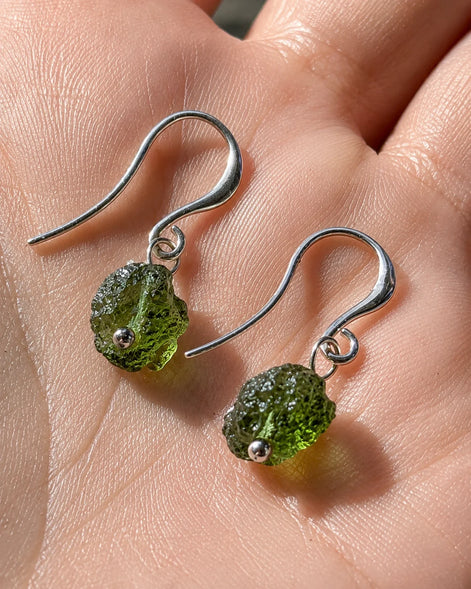 Raw drilled Chlum Moldavite earrings with naturally rounded green stones and rhodium-plated hooks.
