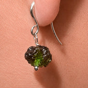 Raw drilled Chlum Moldavite earrings with naturally rounded green stones and rhodium-plated hooks.