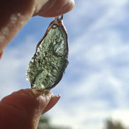 Hand holding a raw Moldavite pendant with a transparent 3.14 g Chlum stone