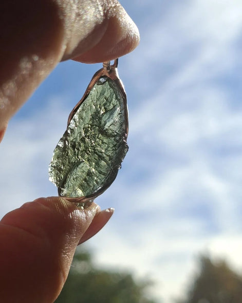 Hand holding a raw Moldavite pendant with a transparent 3.14 g Chlum stone