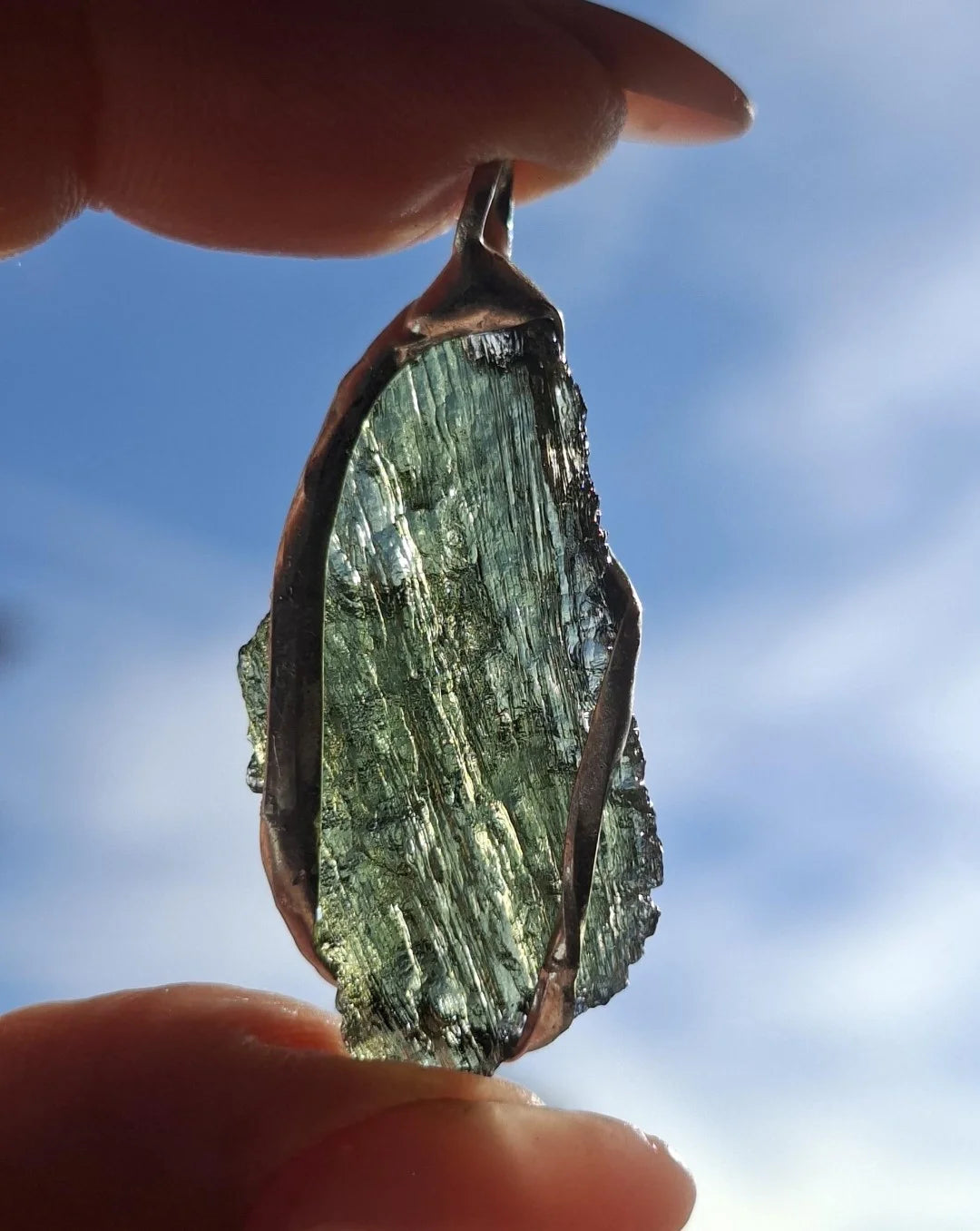 Hand holding a raw Moldavite pendant with a transparent 3.14 g Chlum stone back-side