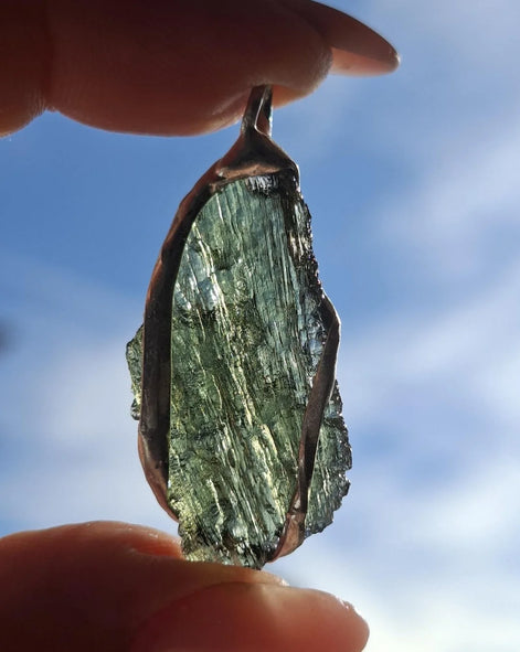 Hand holding a raw Moldavite pendant with a transparent 3.14 g Chlum stone back-side
